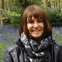 a woman standing among trees with bluebell flowers in the background.